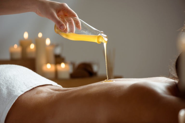 Honey pouring on girl's naked back in spa salon. Copy space.